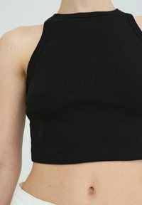 Black ribbed cropped tank top featuring a high neckline and sleeveless design, with a snug fit and textured fabric.