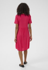Roze jurk met korte mouwen, een aansluitend lijfje en een gathered taille, die net boven de knieën valt. Lichte stof en een ontspannen silhouet.