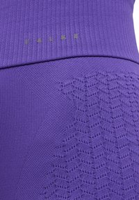Leggings performance viola con motivi testurizzati e sezioni a costine, dotati di un logo metallico "FALKE" vicino alla parte superiore.