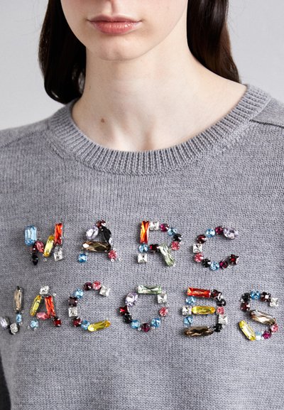 Suéter gris de punto con el nombre "MARC JACOBS" adornado con varias piedras de strass coloridas en diferentes formas y tamaños.