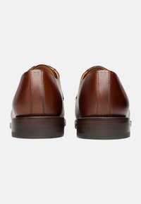 Braune Lederschuhe mit glatter Oberfläche, runder Zehenpartie, flachem Absatz und dezenten Nähten auf der Rückseite. Verstellbares Schnürdesign.