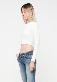 Vit kortärmad topp med lång ärm, kombinerad med ljusblå jeans i denim, som har en urblekt finish och dubbelknappstängning vid midjan.