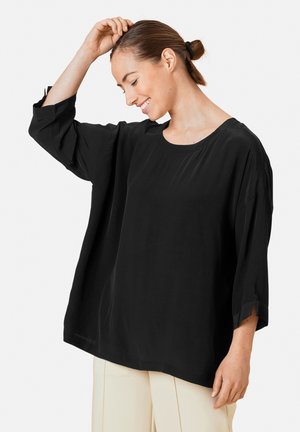 T-shirt noir ample avec manches trois-quarts, encolure ronde et texture subtile. Associé à un pantalon clair.