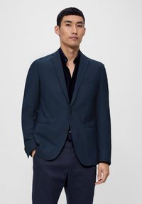 Marineblazer aus strukturiertem Stoff, mitEin-Knopf-Verschluss, Reverskragen und Brusttasche. Trägt man über einem schwarzen Hemd und dunklen Hosen.