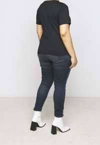 Černé tričko s krátkým rukávem v kombinaci s tmavě modrými skinny džíny, doplněné bílými kotníkovými botami se čtveratým podpatkem. Jednoduchý a přiléhavý design.