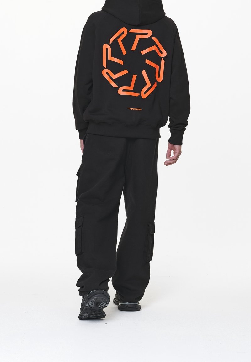 Felpa nera con grande grafica arancione sul retro, abbinata a pantaloni cargo neri. Progettata per il comfort, realizzata in tessuto morbido. Sneakers nere.