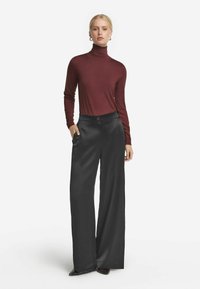 Mörkröd långärmad polotröja kombinerad med vida svarta byxor med knappstängning och sidfickor. Slät tyg med subtil lyster.