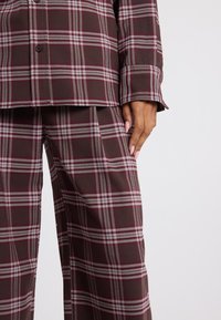 Plaid suit set in dark brown with burgundy and gray stripes. Features a buttoned top and wide-leg pants. Smooth fabric texture.