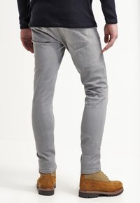 Harmaat slim-fit-housut, joissa on sileä tekstuuri, kaksi takataskua ja huomaamaton kaarrostyö. Yhdistetty ruskeisiin saappaisiin, joissa on nauhakiinnitys.