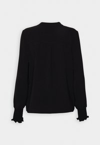 Musta pitkähihainen paita, jossa on pyöreä pääntie, varustettuna keräillyillä hihoilla ja hieman strukturoidulla kankaalla, jossa on takana kaarroke-yksityiskohta.