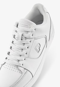 Fehér bőr sneaker, strukturált felülettel, perforált orral, lapos fűzőkkel és diszkrét logóval az oldalon. Minimalista dizájn.