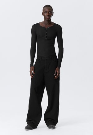 Black long-sleeve henley shirt with four buttons, paired with loose-fitting black trousers. Smooth texture, minimalistic design, and monochrome color.