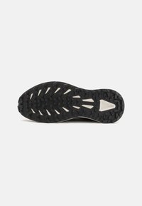 Semelle de chaussure de sport en caoutchouc noir avec un motif de profondeur. Présente des accents blancs et une surface texturée pour une meilleure adhérence.