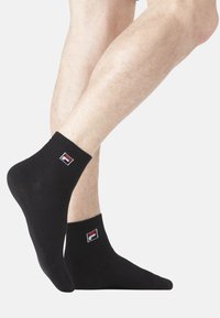 Chaussettes de cheville en coton noir avec un poignet côtelé et un petit logo rouge, blanc et bleu brodé de chaque côté. Texture douce ; design ajusté.