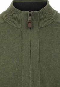 Grüner Strickpullover mit hohem Kragen, ausgestattet mit einem Reißverschluss vorne und gerippten Details am Kragen und den Seiten. Brauner Zipper-Zugakzent.