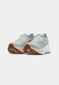 Une paire de chaussures de sport grises claires avec des tiges en maille, des semelles intermédiaires blanches et des semelles extérieures couleur gomme, sur un fond blanc uni.