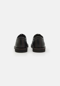 Schwarze Lederschuhe mit flachem Absatz, ausgestattet mit orangen Nähten und einer glatten Textur. Das Design umfasst eine abgerundete Ferse und dezent platzierte Markenkennzeichnung.