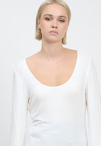 Weißes langärmliges Oberteil mit tiefem Rundhalsausschnitt, aus glattem Stoff gefertigt. Verfügt über eine figurbetonte Silhouette und ein minimalistisches Design.