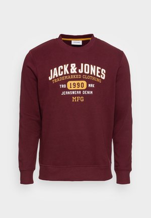 Sweat-shirt col rond bordeaux avec les inscriptions "JACK & JONES," "1990," et "JEANSWEAR DENIM MFG" imprimées en jaune et blanc sur la poitrine.