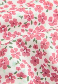 Vitt tyg med ett livligt rosa blommönster och gröna blad. Blommorna varierar i storlek och är tätt placerade över ytan.
