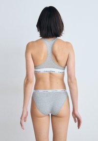 Szürke pamut sportmelltartó és hozzá illő bikini alsó fehér Calvin Klein logós pánttal. Racerback dizájn; sima, testhezálló textúra.