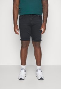 Czarne dżinsowe szorty z podwiniętymi nogawkami, noszone z turkusową koszulą i białymi trampkami. Projekt obejmuje standardowe kieszenie i dopasowaną sylwetkę.