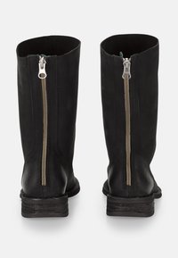 Par de botas negras de cuero hasta la mitad de la pantorrilla con cremalleras plateadas visibles que corren verticalmente por la parte trasera y tacones bajos apilados.