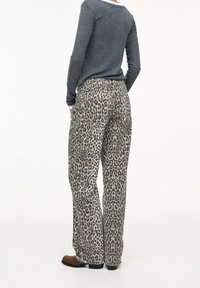 Pantalones de estampado de leopardo en una tela suave y texturizada, con un corte holgado, bolsillos traseros y una cintura alta. Combinados con una blusa de manga larga gris.