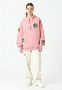 Rosa huvtröja med sol- och månmotiv, med en framfick och ribbad mudd, kombinerad med krämfärgade cargobyxor och vita sneakers.