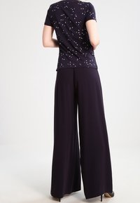 Mörkblå kortärmad topp med vitt abstrakt mönster, ihopparad med lösa, vida mörka byxor. Slätt tyg med subtil textur.