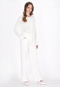 Cardigan bianco a maglia con chiusura a bottoni, caratterizzato da un design testurizzato. Abbinato a pantaloni bianchi dal taglio morbido e tacchi a punta.