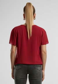 Rode blouse met korte, transparante mouwen, met een relaxte pasvorm en een ronde halslijn, gecombineerd met donkergrijze jeans. Soepele textuur.