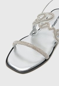 Silver flat sandal featuring a metallic upper with embellished straps, a square toe shape, and a smooth, reflective texture.