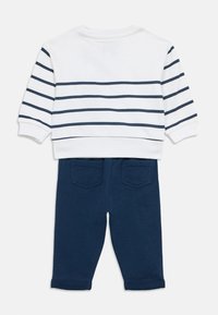 Λευκό πουκάμισο με μακριά μανίκια και οριζόντιες ναυτικές ρίγες, συνδυασμένο με ναυτικό παντελόνι με πίσω τσέπες και γυρισμένα μανίκια.