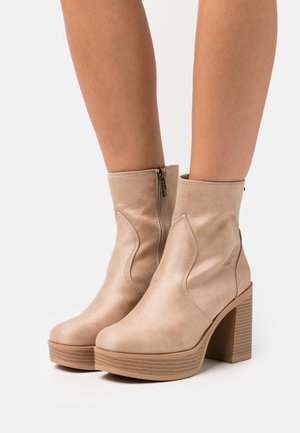 Bottines en cuir beige avec une finition texturée, un talon épais et des coutures décoratives sur les côtés. Fermeture éclair à l'arrière.