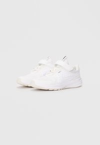 Des chaussures de sport blanches avec une tige en mesh, une sangle ajustable et une semelle texturée avec un motif de petites étoiles sur les côtés.