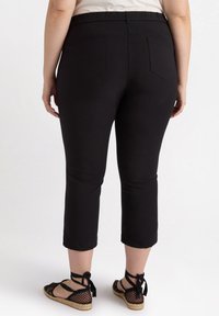 Zwarte stretchpants met een elastische tailleband, cropped lengte en twee achterzakken, gecombineerd met zwarte espadrille sandaaltjes met bandjes.