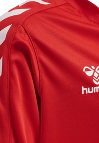 Rød atletisk trøje med en glat tekstur, der har hvide accentstriber på skuldrene og et logo i hvidt på brystet.