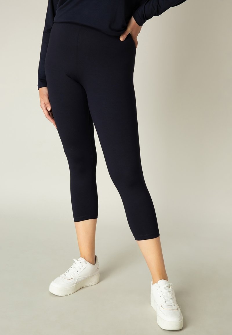 Donkerblauwe cropped leggings van rekbare stof, met een gladde textuur en een strakke pasvorm, gecombineerd met witte platform sneakers.