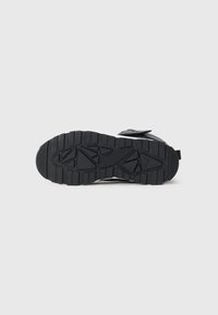 Svart gummisula på en sneaker med spår och triangulära mönster, visad mot en ren vit bakgrund.