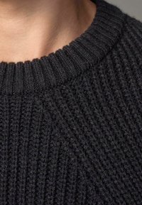 Gros plan sur un pull en maille gris foncé texturé, avec un col côtelé et mettant en valeur le motif de tricot doux.