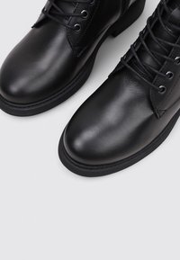 Bottines en cuir noir avec bouts ronds, design à lacets, œillets en métal et semelles en caoutchouc texturé. Fini lisse avec un minimum de coutures.