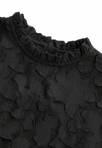 Tissu noir avec maille transparente et grand motif d'appliqué floral, avec un col froncé et plissé.