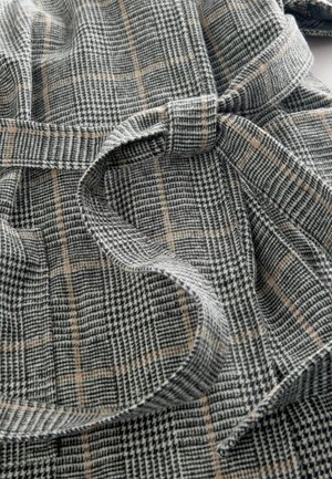 Szürke, fekete és bézs kockás szövet. Puha tapintású anyag, kötött derékpánttal. Mintái között megtalálható a solymász- és a kockás minta, vizuális érdeklődést keltve.