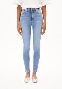 Jean skinny taille haute bleu clair en denim à texture lisse avec une décoloration minimale ; orné d'un bouton et de deux poches avant.
