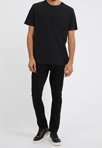 Černé tričko s vyraženým logem, kulatým výstřihem a krátkými rukávy, spárované s černými slim-fit kalhotami a černými teniskami s bílou podrážkou.