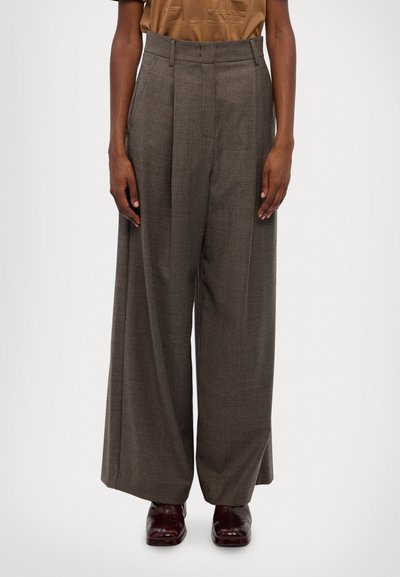 Pantalones de pierna ancha en un patrón de cuadros marrón, con cintura alta y pliegues, confeccionados en una tela texturizada. Combinados con zapatos oscuros pulidos.