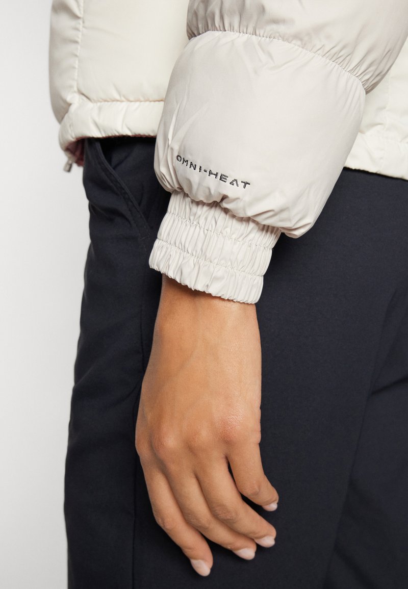 Chaqueta acolchada de color claro con puños elásticos. Presenta la marca Omni-Heat en el puño. Textura suave, diseño aislante para mantener el calor.