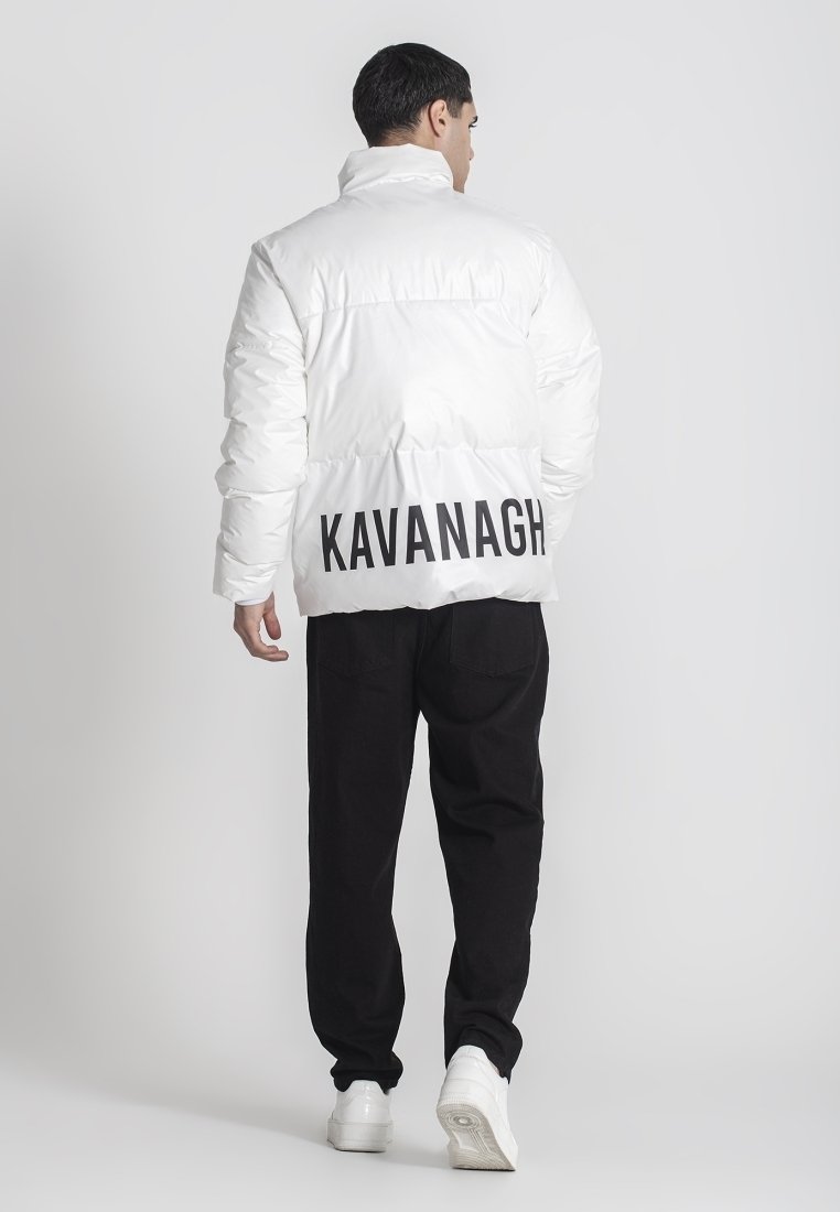 Biela vypchávkovaná bunda s vysokým golierom a logom "KAVANAGH" na chrbte. Skombinovaná s čiernymi nohavicami a bielymi teniskami. Hladká, lesklá textura.