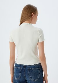 Top corto a maniche corte a coste in bianco sporco con collo scallop, abbinato a jeans in denim blu a vita alta.